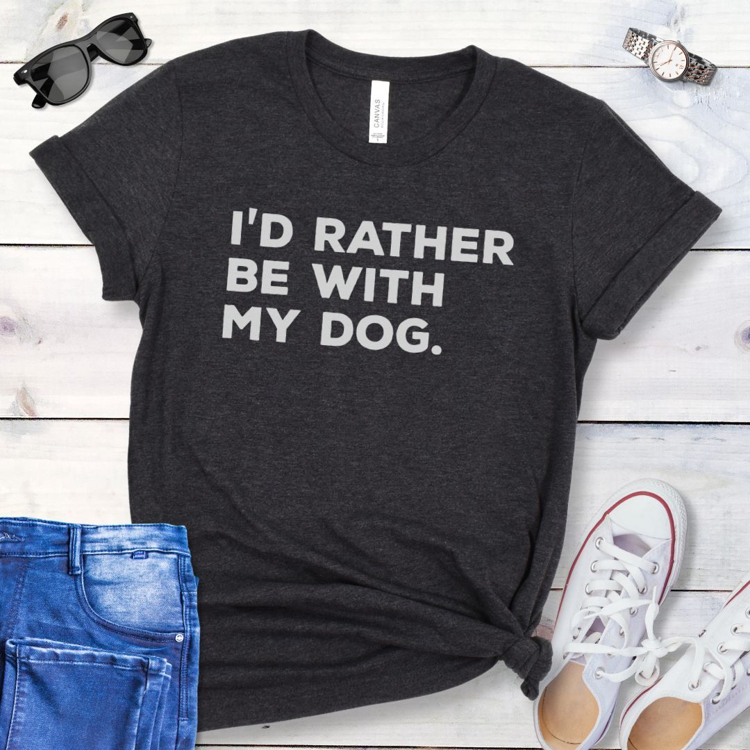 Dark grey t-shirt for dog lovers with 'I'd Rather Be With My Dog' text in bold lettering, shown on a wooden surface with jeans and shoes.