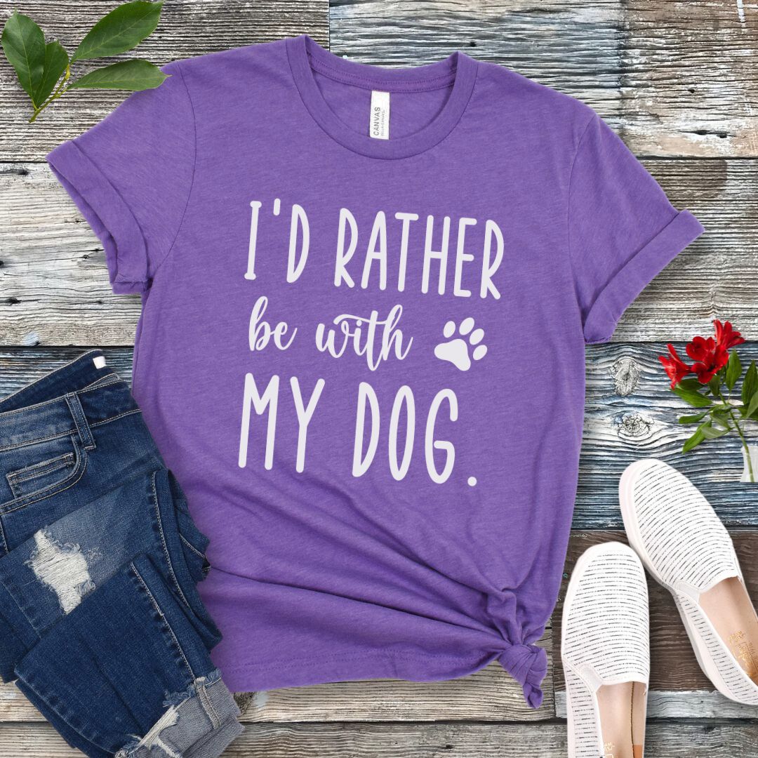 Purple t-shirt with 'I'd rather be with my dog' text on a wooden surface with jeans and shoes.
