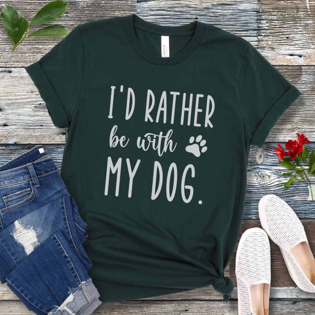 Dark green t-shirt with 'I'd rather be with my dog' text on a wooden surface with jeans and shoes.