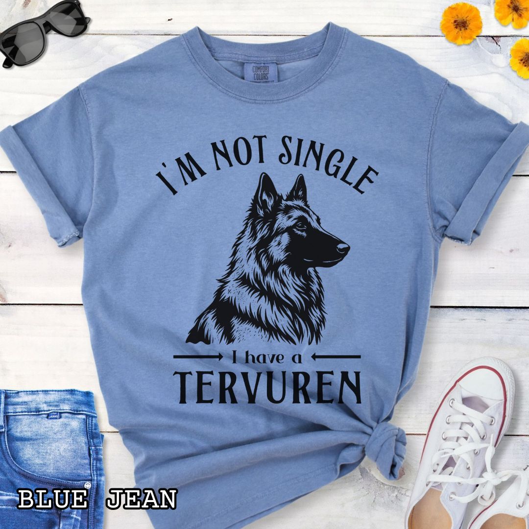 Blue Comfort Colors t-shirt with a woodcut-style Belgian Tervuren graphic and humorous text 'I'm Not Single, I Have a Belgian', shown on a wooden surface with jeans and sneakers.