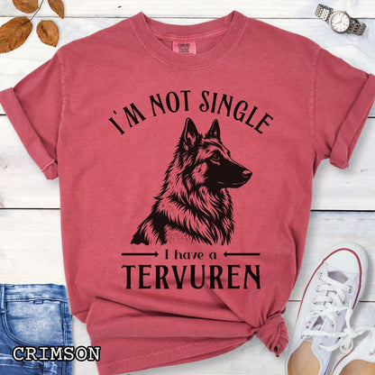 Red Comfort Colors t-shirt with a woodcut-style Belgian Tervuren graphic and humorous text 'I'm Not Single, I Have a Belgian', shown on a wooden surface with jeans and sneakers.