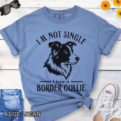Blue Comfort Colors t-shirt with a Border Collie graphic and humorous text 'I'm Not Single, I Have A Border Collie', shown on a wooden surface with jeans and shoes.