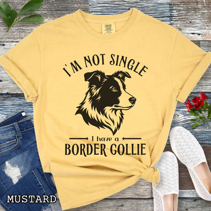 Mustard yellow Comfort Colors t-shirt with a Border Collie graphic and humorous text 'I'm Not Single, I Have A Border Collie', shown on a wooden surface with jeans and shoes.