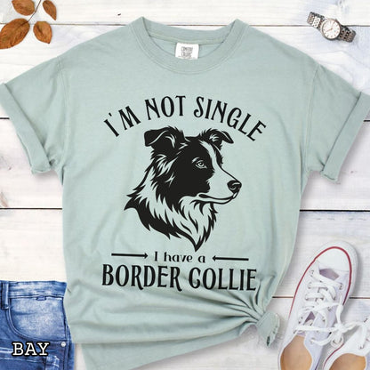Light green Comfort Colors t-shirt with a Border Collie graphic and humorous text 'I'm Not Single, I Have A Border Collie', shown on a wooden surface with jeans and shoes.