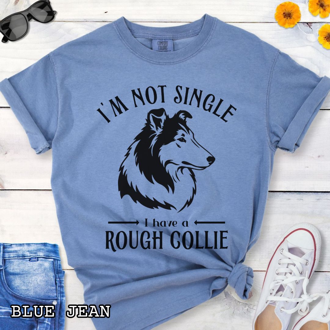 Blue Comfort Colors t-shirt with a Rough Collie graphic and humorous text 'I'm Not Single, I Have a Rough Collie', shown on a wooden surface with accessories.