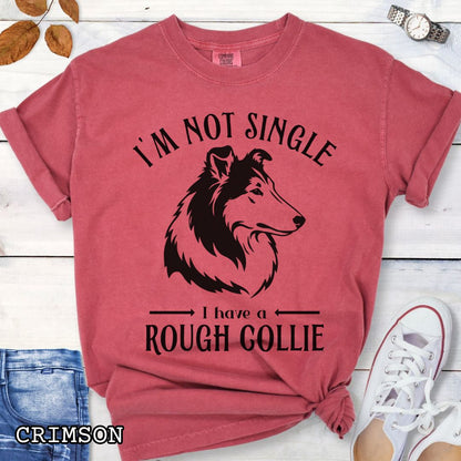 Red Comfort Colors t-shirt with a Rough Collie graphic and humorous text 'I'm Not Single, I Have a Rough Collie', shown on a wooden surface with accessories.