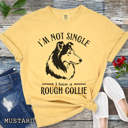 Mustard yellow Comfort Colors t-shirt with a Rough Collie graphic and humorous text 'I'm Not Single, I Have a Rough Collie', shown on a wooden surface with accessories.
