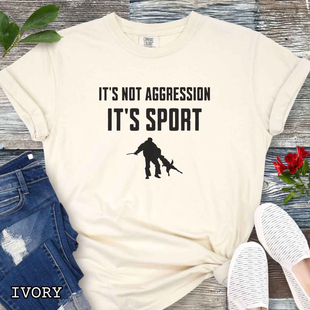Beige Comfort Colors t-shirt for Schutzhund/IGP bitework dog trainers with 'It's not aggression, it's sport' text and a bite work graphic, shown on a wooden surface.