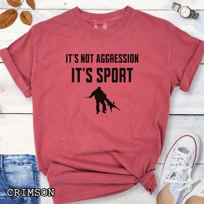 Red Comfort Colors t-shirt for Schutzhund/IGP bitework dog trainers with 'It's not aggression, it's sport' text and a bite work graphic, shown on a wooden surface.