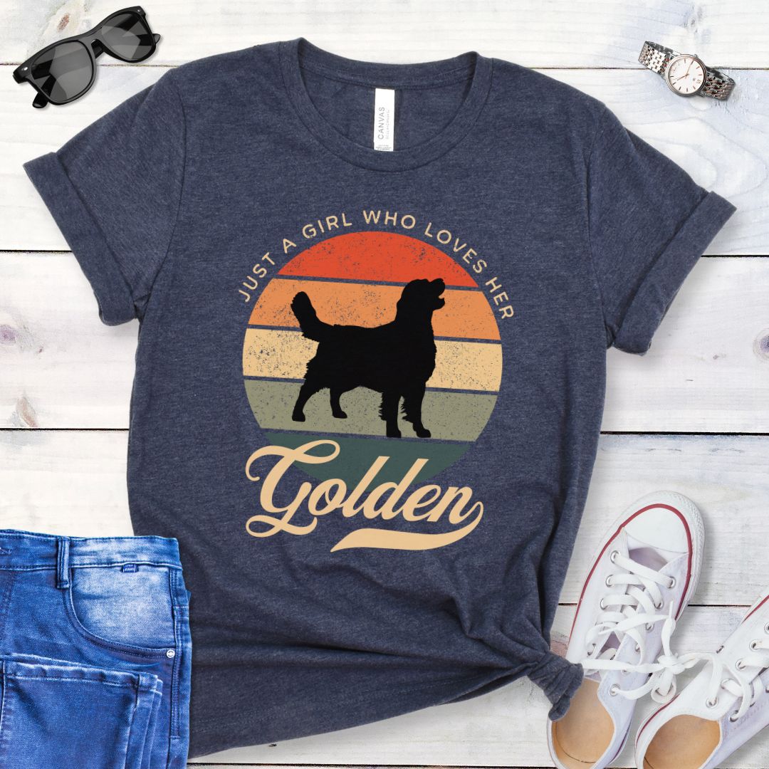 Heather navy t-shirt with vintage sunset graphic, a Golden Retriever silhouette, and the text 'Just a girl who loves her Golden', presented on a wooden surface with jeans and shoes.