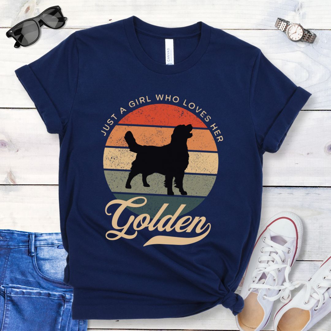 Navy blue t-shirt with vintage sunset graphic, a Golden Retriever silhouette, and the text 'Just a girl who loves her Golden', presented on a wooden surface with jeans and shoes.
