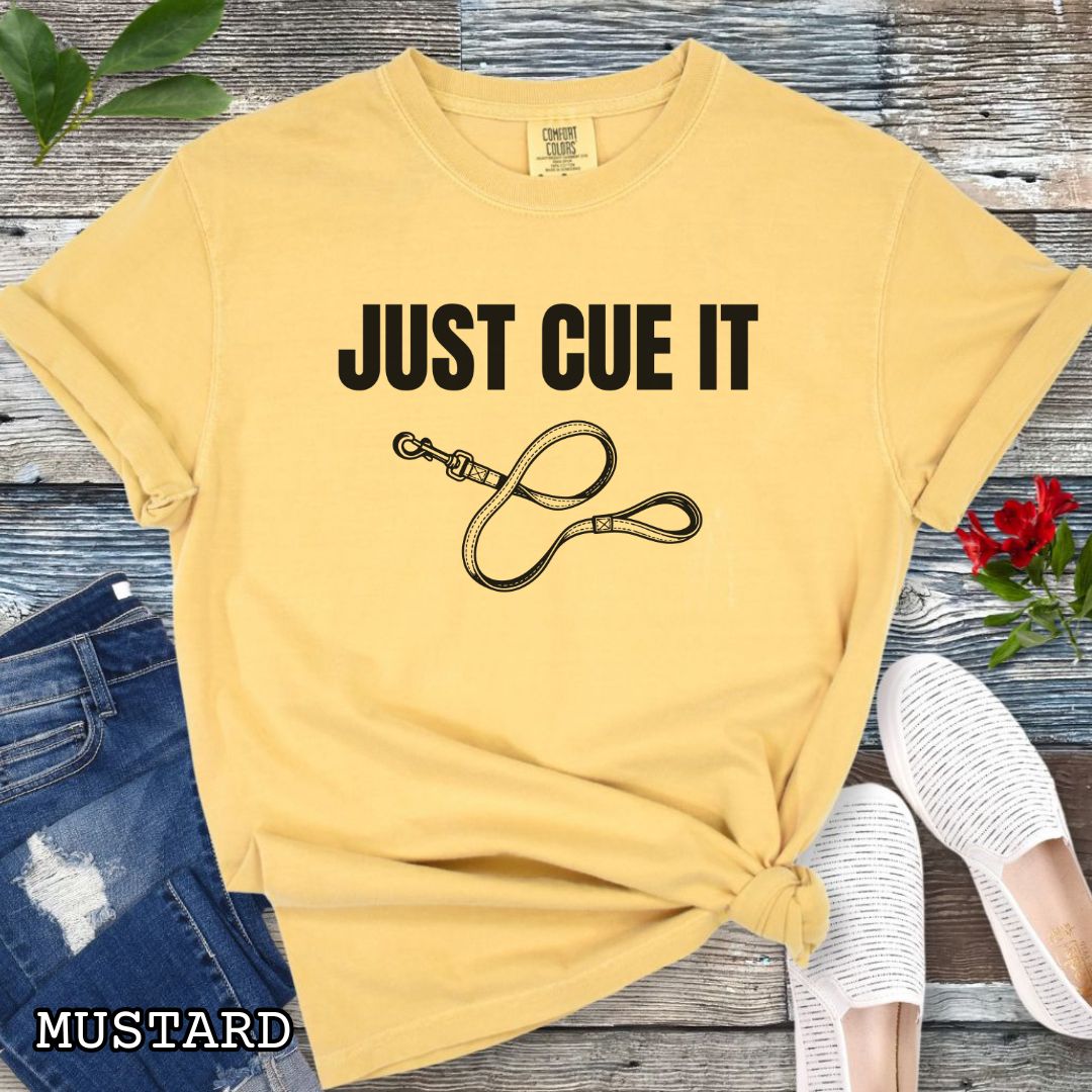 Mustard yellow Comfort Colors t-shirt featuring a Just Cue It text with leash graphic, a positive reinforcement dog training shirt for dog trainers and reward-based training enthusiasts.