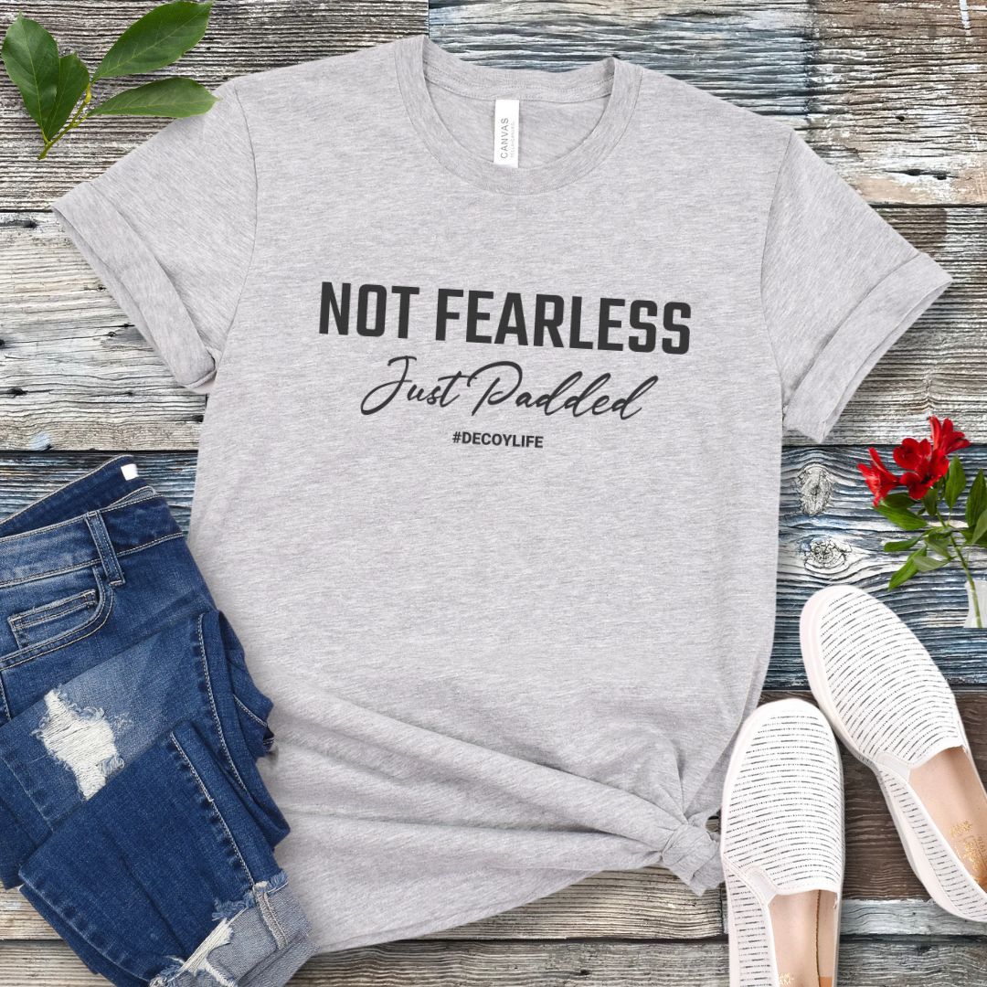 Athletic Grey K9 helper t-shirt with 'Not Fearless Just Padded, #decoylife' text on a wooden surface with jeans and shoes.