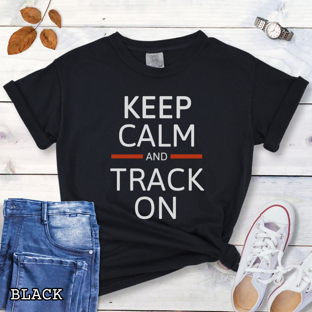 Black dog tracking training t-shirt with 'Keep Calm and Track On' in bold text on a wooden surface with jeans and sneakers.