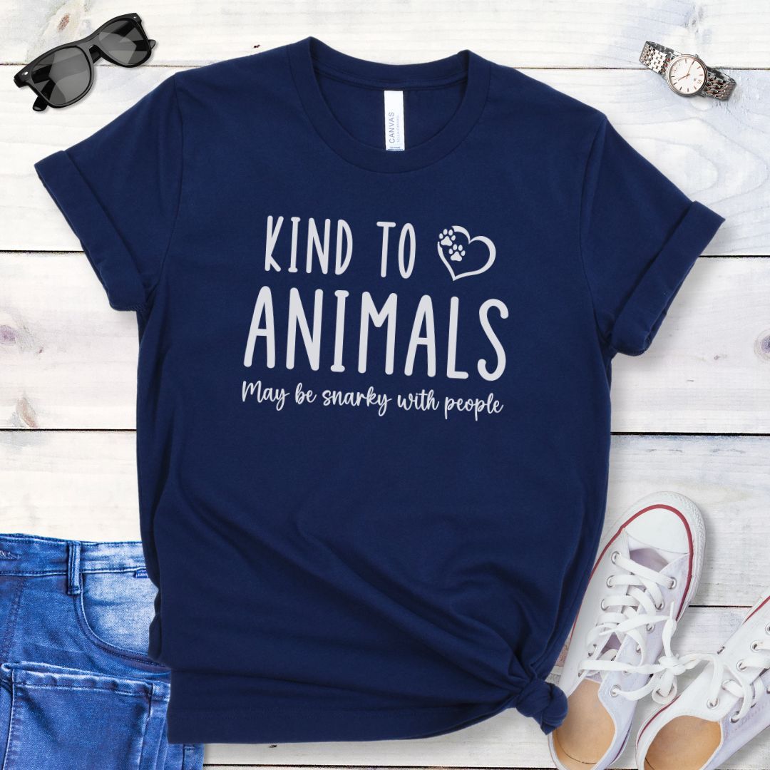 Navy blue unisex t-shirt for pet and animal lovers with humorous text 'Kind to Animals May be snarky with people' in playful lettering, shown on a wooden surface with accessories.