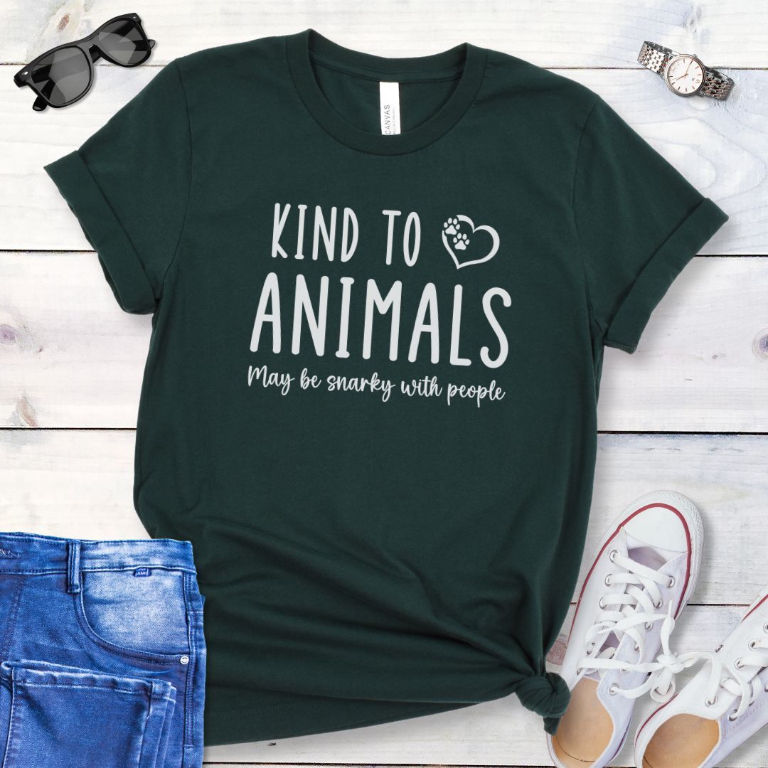 Green unisex t-shirt for pet and animal lovers with humorous text 'Kind to Animals May be snarky with people' in playful lettering, shown on a wooden surface with accessories.