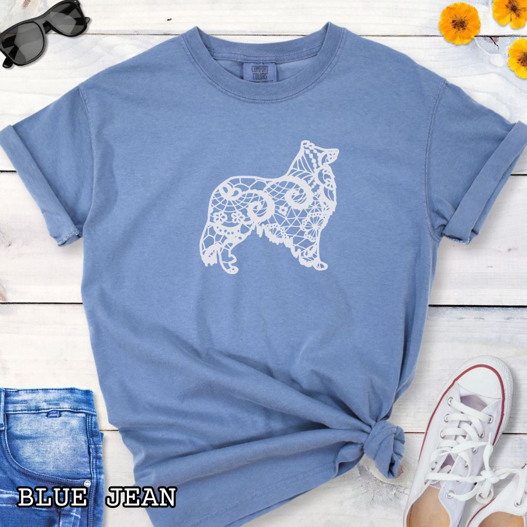 Blue Comfort Colors t-shirt with a white  Rough Collie silhouette filled with faux-lace pattern, shown on a wooden surface with shoes and jeans.