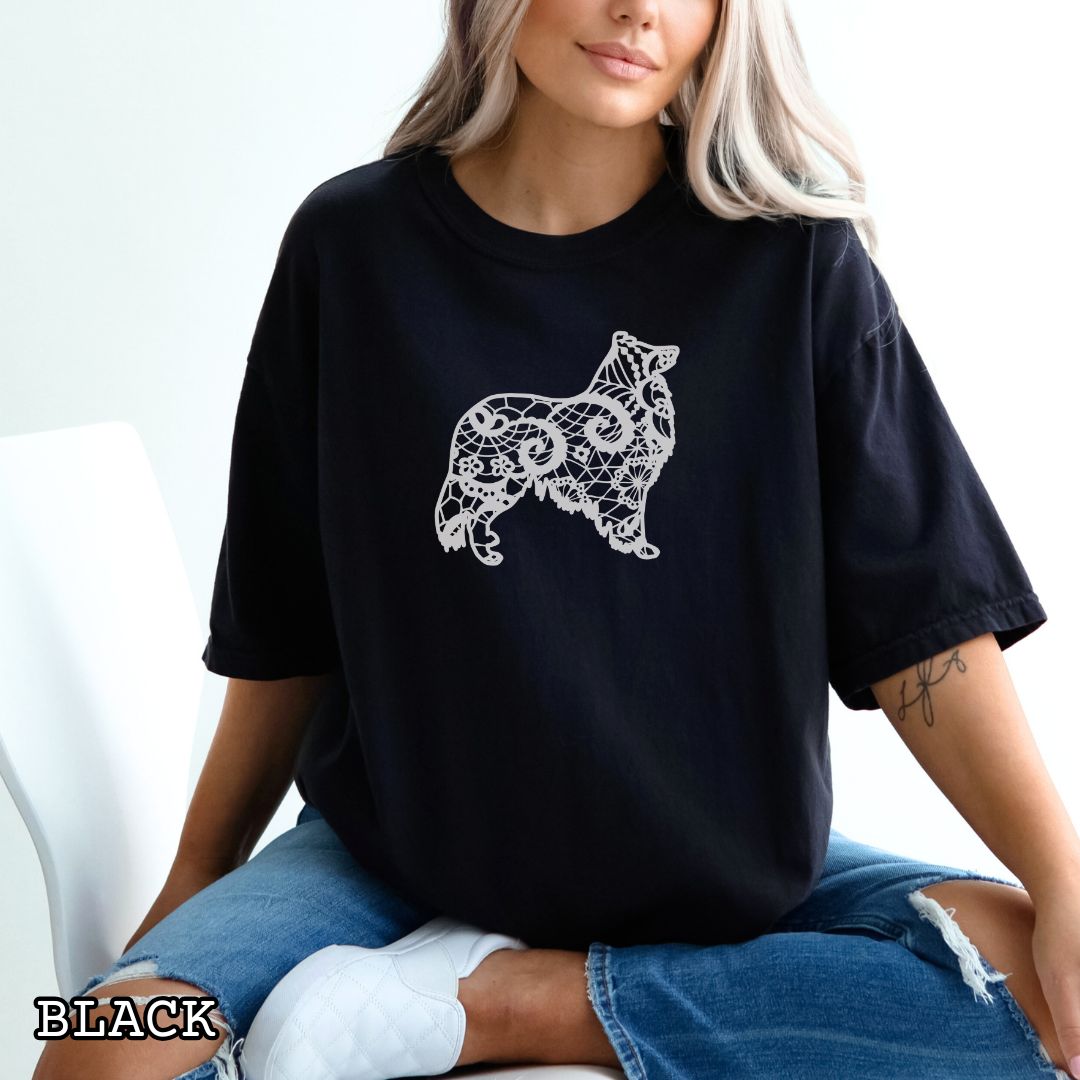 Person wearing a black Comfort Colors t-shirt with a white  Rough Collie silhouette filled with faux-lace pattern, shown on a wooden surface with shoes and jeans.