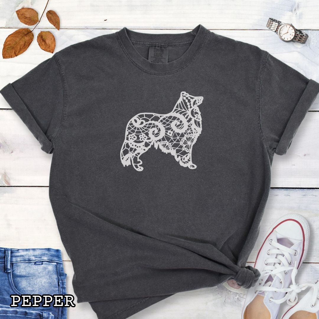 Dark gray Comfort Colors t-shirt with a white  Rough Collie silhouette filled with faux-lace pattern, shown on a wooden surface with shoes and jeans.