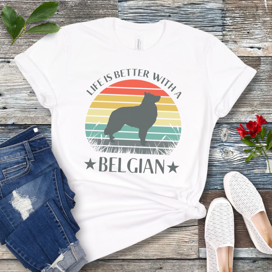 White t-shirt for Belgian Sheepdog lovers with a retro sunset graphic design featuring a Belgian Sheepdog silhouette and text 'Life is better with a Belgian', shown on a wooden surface.