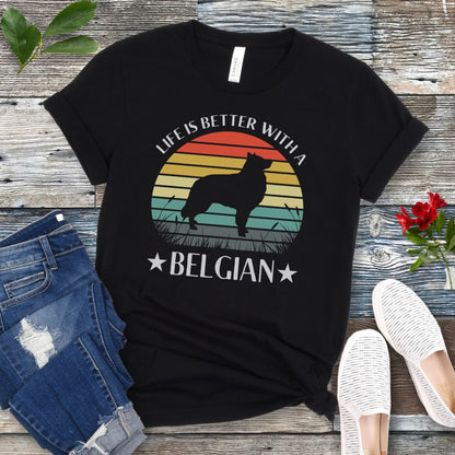 Black t-shirt for Belgian Sheepdog lovers with a retro sunset graphic design featuring a Belgian Sheepdog silhouette and text 'Life is better with a Belgian', shown on a wooden surface.