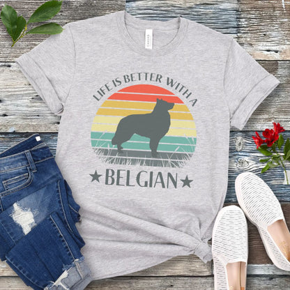 Grey t-shirt for Belgian Sheepdog lovers with a retro sunset graphic design featuring a Belgian Sheepdog silhouette and text 'Life is better with a Belgian', shown on a wooden surface.