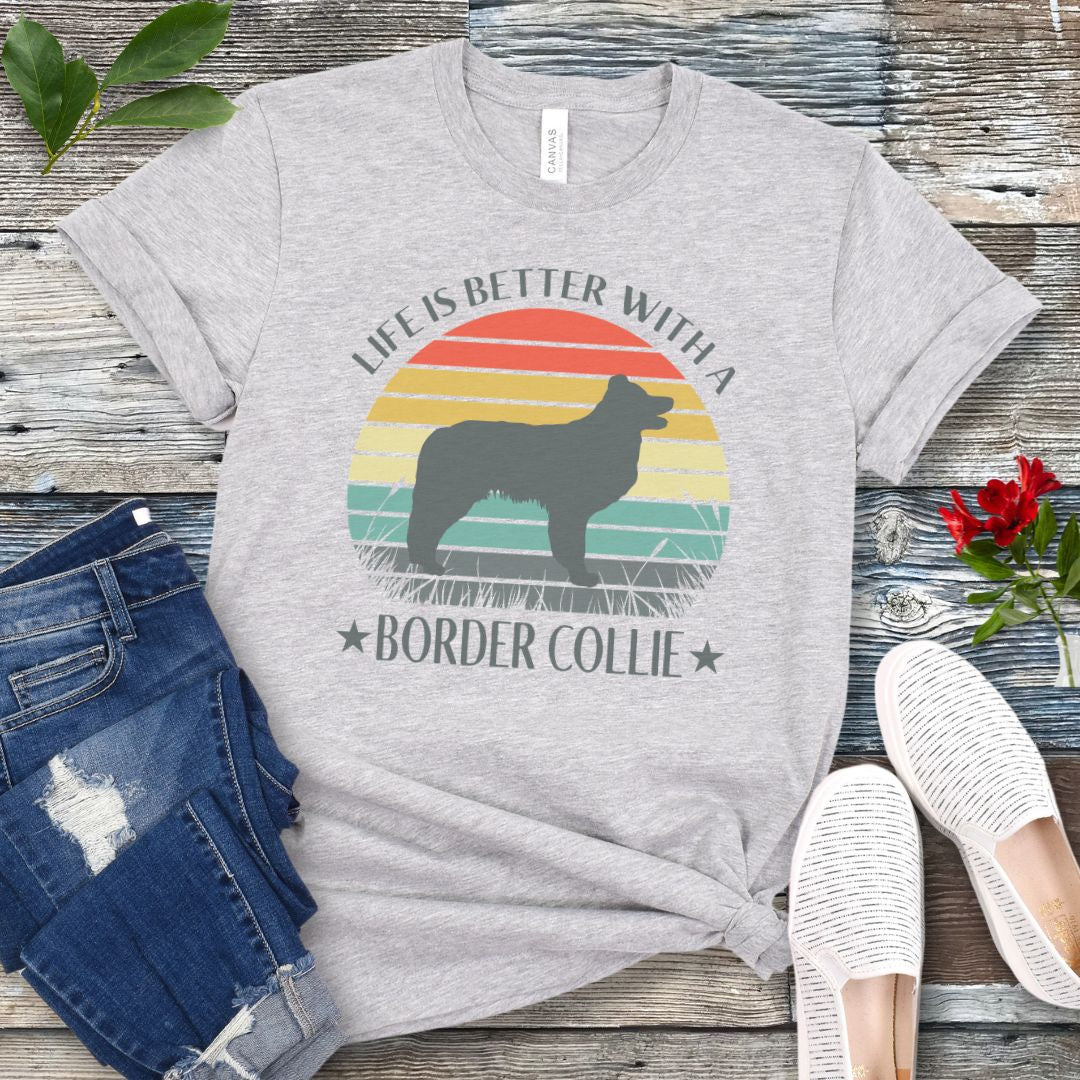Grey t-shirt with a vintage sunset graphic with a Border Collie and the text  'Life is Better With A Border Collie', shown on a wooden surface with jeans and sneakers.