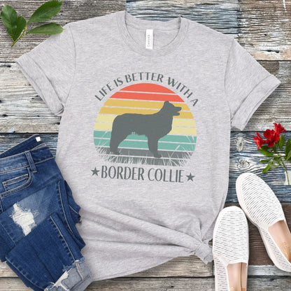 Grey t-shirt with a vintage sunset graphic with a Border Collie and the text  'Life is Better With A Border Collie', shown on a wooden surface with jeans and sneakers.