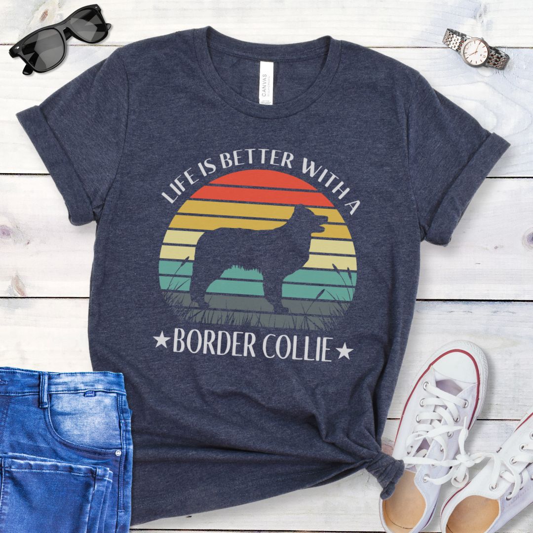 Navy blue t-shirt with a vintage sunset graphic with a Border Collie and the text  'Life is Better With A Border Collie', shown on a wooden surface with jeans and sneakers.