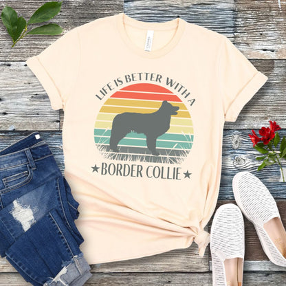 Beige t-shirt with a vintage sunset graphic with a Border Collie and the text  'Life is Better With A Border Collie', shown on a wooden surface with jeans and sneakers.