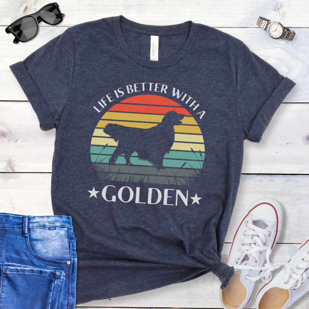 Heather navy t-shirt with a Golden Retriever dog graphic in a vintage sunset design, with the text 'Life Is Better With a Golden', shown on a wooden surface with jeans and shoes.