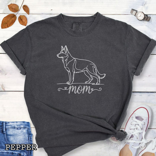 Dark grey Comfort Colors t-shirt for German Shepherd lovers, with elegant line art German Shepherd dog graphic and 'mom' text below it in script lettering, shown on a wooden surface.