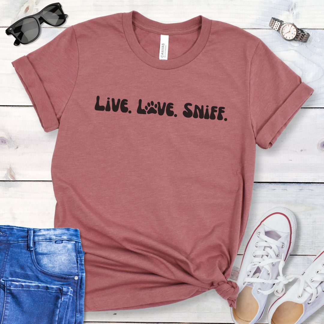 Mauve canine scent work t-shirt with 'Live. Love. Sniff.' text in retro font, presented on a wooden surface with jeans and shoes.