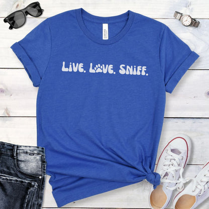 Blue canine scent work t-shirt with 'Live. Love. Sniff.' text in retro font, presented on a wooden surface with jeans and shoes.
