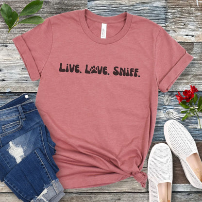 Mauve canine scent work t-shirt with 'Live. Love. Sniff.' text in retro font, presented on a wooden surface with jeans and shoes.