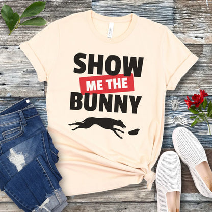 Beige lure coursing t-shirt with bold 'Show Me The Bunny' text and sighthound graphic on a wooden surface with jeans and shoes.