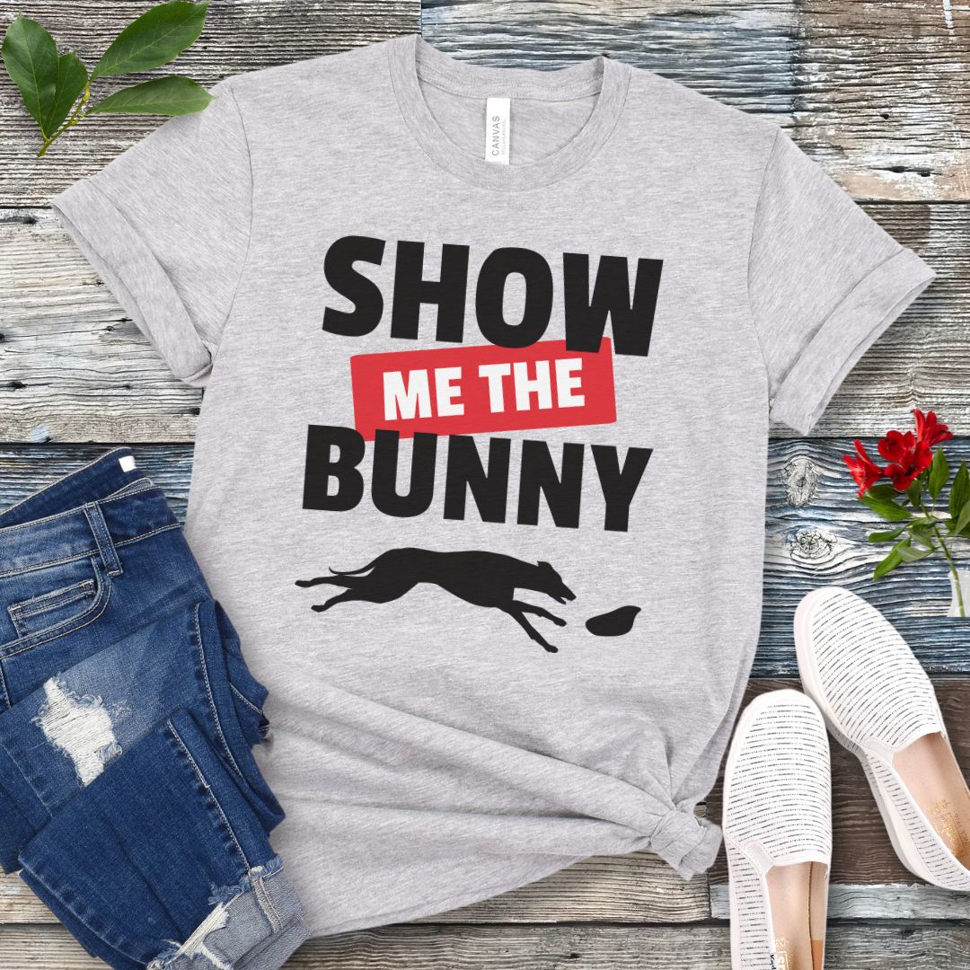 Grey lure coursing t-shirt with bold 'Show Me The Bunny' text and sighthound graphic on a wooden surface with jeans and shoes.