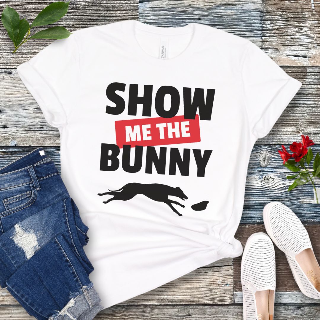 White lure coursing t-shirt with bold 'Show Me The Bunny' text and sighthound graphic on a wooden surface with jeans and shoes.