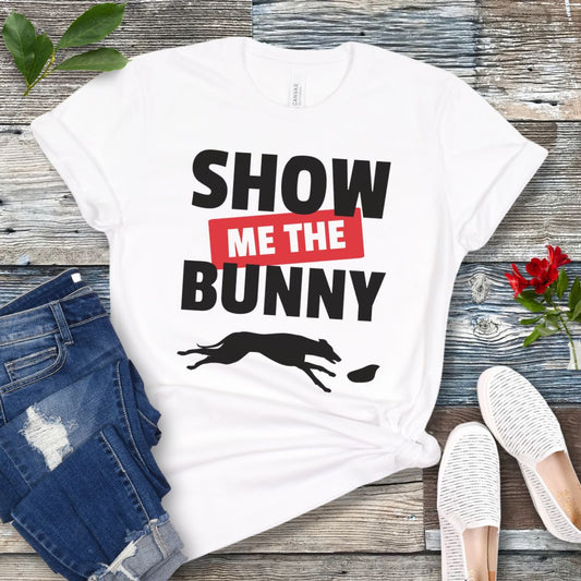 White lure coursing t-shirt with bold 'Show Me The Bunny' text and sighthound graphic on a wooden surface with jeans and shoes.