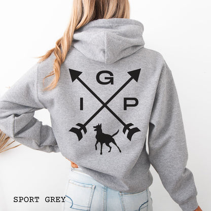Grey Schutzhund/IGP hoodie with crossed arrows design with 'IGP' text and Belgian Malinois on the back, presented on a wooden surface with accessories.