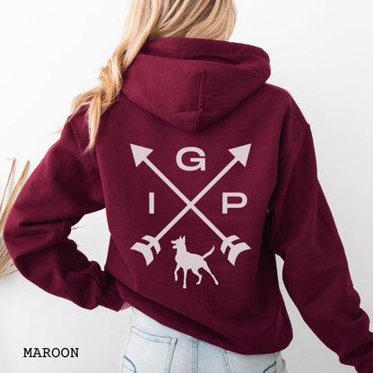 Maroon Schutzhund/IGP hoodie with crossed arrows design with 'IGP' text and Belgian Malinois on the back, presented on a wooden surface with accessories.