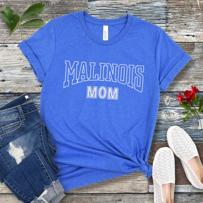 A royal blue Bella Canvas 3001 unisex short sleeve T-shirt with 'MALINOIS MOM' printed in college style lettering, displayed on a wooden surface with denim jeans and white shoes in the background.