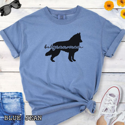 Blue Comfort Colors t-shirt with Belgian Sheepdog silhouette and 'Belgian Mom' text in handwritten script lettering, shown on a wooden surface with denim jeans and a flower.
