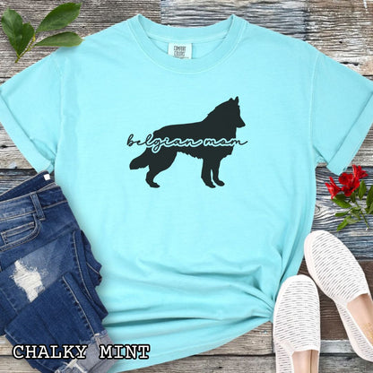 Mint Comfort Colors t-shirt with Belgian Sheepdog silhouette and 'Belgian Mom' text in handwritten script lettering, shown on a wooden surface with denim jeans and a flower.