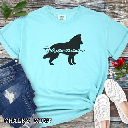 Mint Comfort Colors t-shirt with Belgian Tervuren silhouette and 'Terv Mom' text in handwritten script lettering, shown on a wooden surface with denim jeans and a flower.