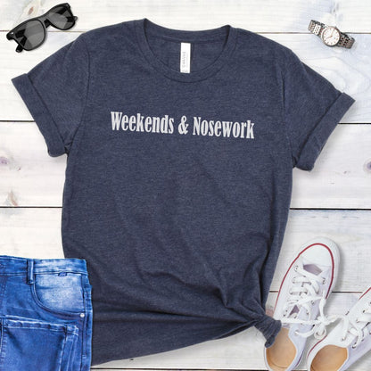 Navy blue t-shirt for K9 Nose Work trainer with 'Weekends & Nosework' text on a wooden surface with jeans, sneakers, and sunglasses.