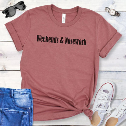 Mauve t-shirt for K9 Nose Work trainer with 'Weekends & Nosework' text on a wooden surface with jeans, sneakers, and sunglasses.