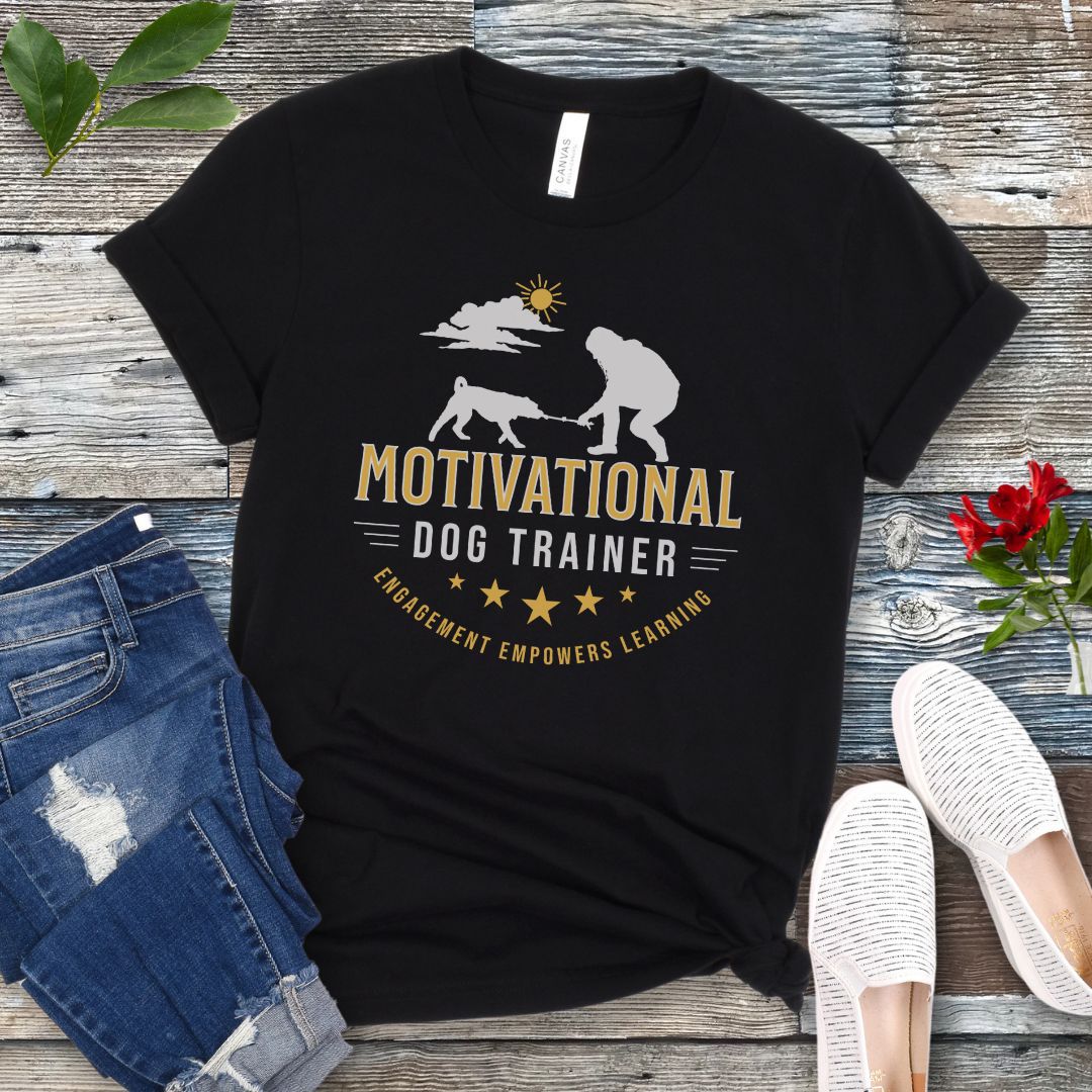 Black t-shirt with 'Motivational Dog Trainer' graphic on a wooden surface with jeans and shoes.