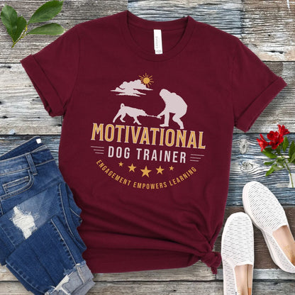 Maroon t-shirt with 'Motivational Dog Trainer' design on a wooden surface with jeans and shoes.