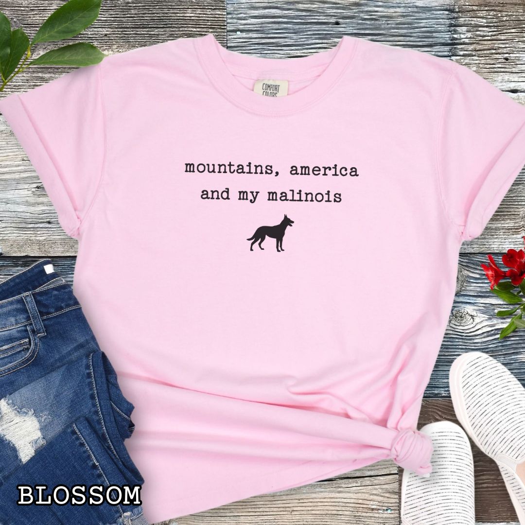 Pink Comfort Colors Belgian Malinois t-shirt with minimalist 'mountains, America and my malinois' quote and Malinois dog silhouette, perfect for patriotic dog lovers, hiking enthusiasts, working dog handlers, and adventurous Malinois owners. Great gift for Belgian Malinois moms, outdoorsy dog owners, and canine sport fans who love life with their loyal companion.